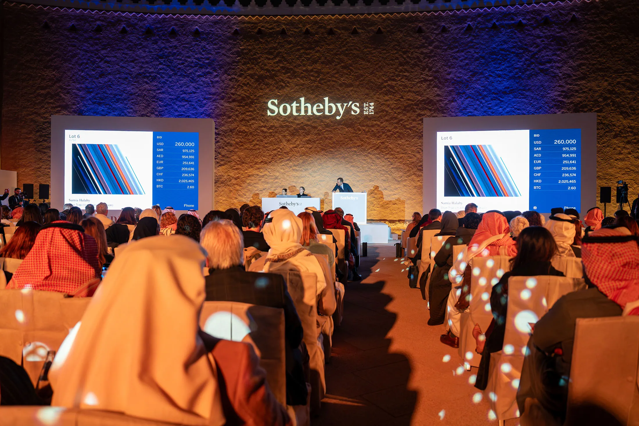 Sotheby’s Saudi Arabia auction event featuring digital art sales, with cryptocurrency bidding options displayed on large screens.
