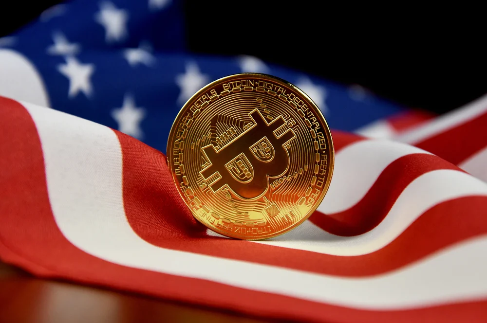 A Bitcoin coin standing on an American flag, symbolising the relationship between cryptocurrency and U.S. financial and regulatory policies.